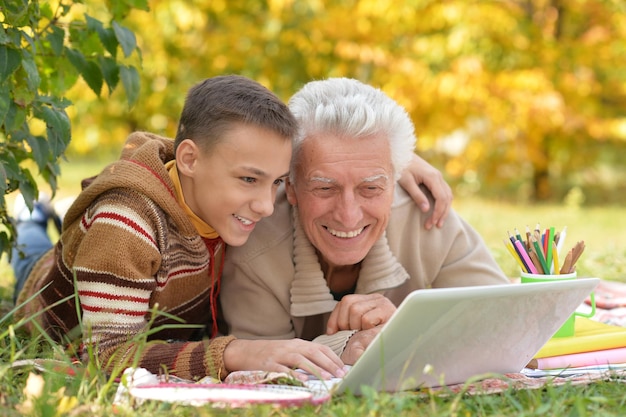 Ritratto di ragazzo e nonno con un computer portatile nel parco