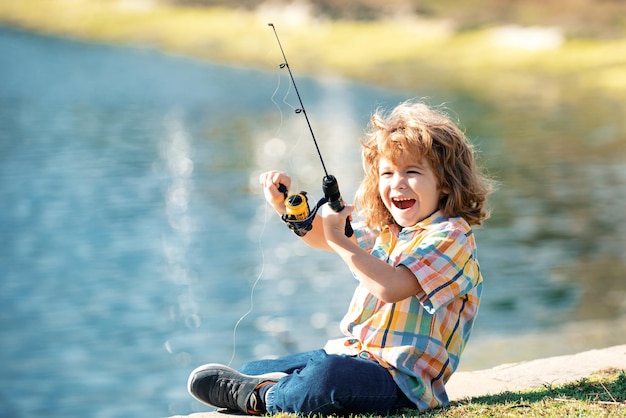 Ritratto di ragazzo eccitato che pesca Eccitato bambino sorpreso seduto vicino al lago e pesca