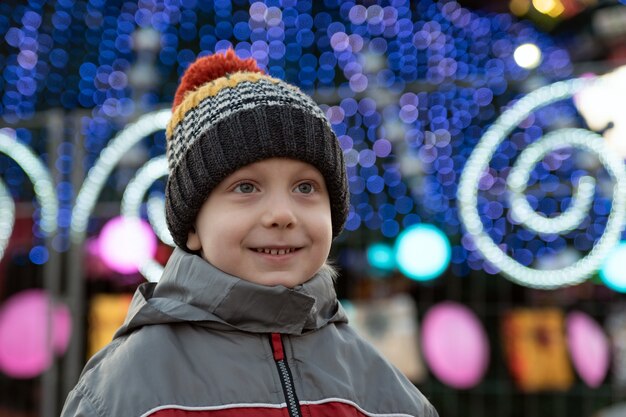 Ritratto di ragazzo in cappello lavorato a maglia sullo sfondo di decorazioni di Capodanno sulla strada.