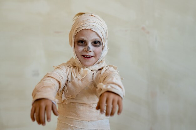 Ritratto di ragazzo positivo in costume da mummia fatto di bende che si comportano come zombie alla festa di Halloween