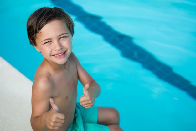 Ritratto di ragazzo sorridente che mostra i pollici in su a bordo piscina