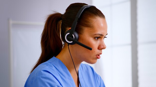 Ritratto di receptionist medico che risponde premendo sulla cuffia aiutando il paziente a fissare un appuntamento in ospedale. Medico sanitario in uniforme medica, assistente medico durante la comunicazione di telemedicina