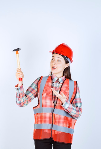 Ritratto di riparatore femminile in uniforme in piedi con martello sul muro bianco.