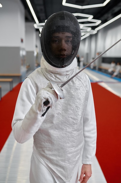 Ritratto di schermidore adolescente che indossa uniforme in posa con la spada per la macchina fotografica. Concetto di arte marziale di scherma e scherma