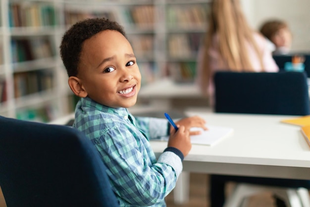 Ritratto di scolaro afroamericano seduto alla scrivania in aula che torna indietro e sorride a