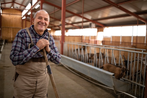 Ritratto di senior cattleman con forcone in piedi in casa colonica