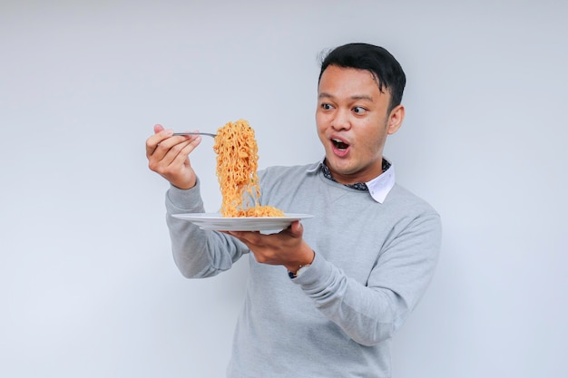 Ritratto di Shock e Wow Il giovane uomo asiatico si diverte con i noodles Mangiare il concetto di pranzo