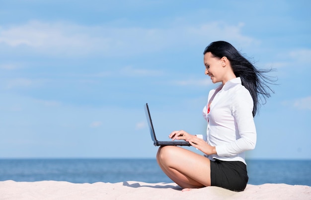 Ritratto di signora dell'ufficio con il computer portatile in spiaggia