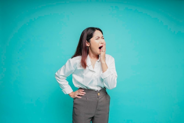 Ritratto di sonnolenta donna asiatica attraente che indossa una camicia bianca che si sente stanca dopo la notte senza dormire sbadigliando coprendo la bocca aperta con il palmo