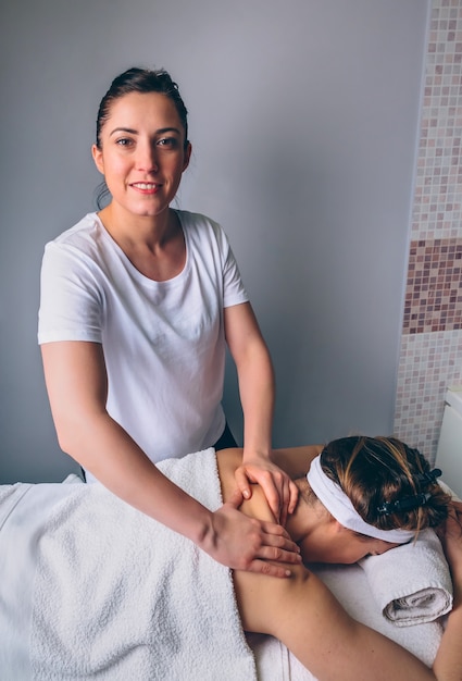 Ritratto di sorridente massaggiatore femminile facendo massaggio rilassante sulle spalle della giovane donna in un centro clinico. Medicina, sanità e concetto di bellezza.