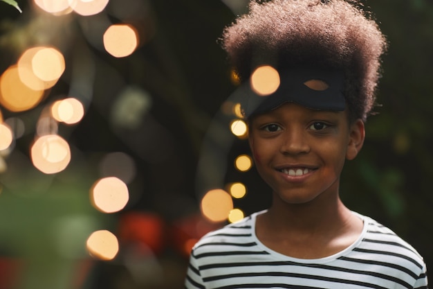 Ritratto di sorridente ragazzo afro-americano durante la festa di Halloween all'aperto con luci, copia spazio