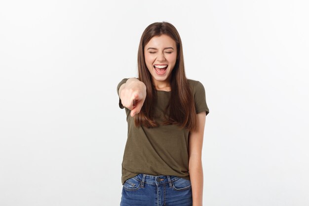 Ritratto di sorriso attraente ridere ragazza adolescente, puntando il dito, indossare camicia verde, denti bianchi, capelli lunghi castani, isolato su bianco.