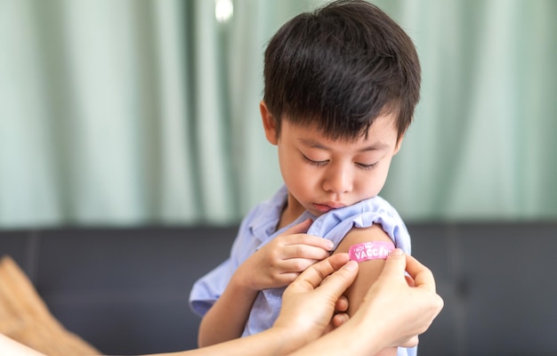 Ritratto di sorriso felice vaccinato ragazzino asiatico bambini di età compresa tra 5 e 11 anni in posa mostra braccio con cerotto medico dopo il vaccino iniettabile protezione Covid19 vaccinazione contro il coronavirus bambino