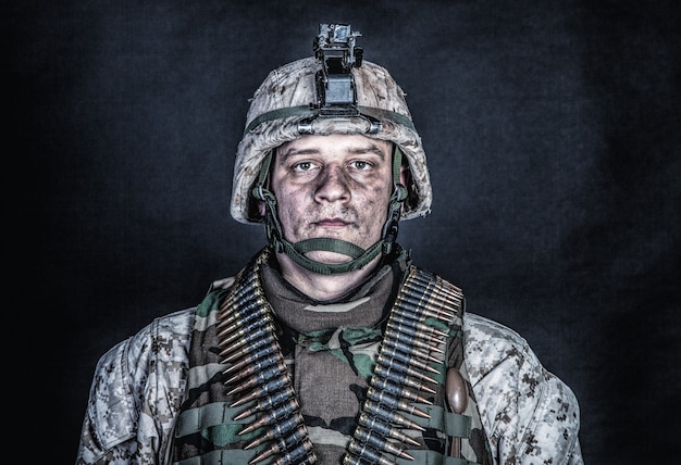 Ritratto di spalla di soldato esperto dell'esercito, veterano di conflitti militari, abile combattente marino in uniforme mimetica cenciosa, casco avanzato e cinture di munizioni sul petto, girato in studio su sfondo nero