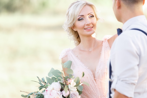 Ritratto di sposi sulla natura nel giorno d'estate. la sposa e lo sposo che abbracciano al matrimonio.