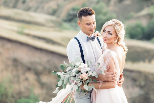 Ritratto di sposi sulla natura nel giorno d'estate. la sposa e lo sposo che abbracciano al matrimonio.