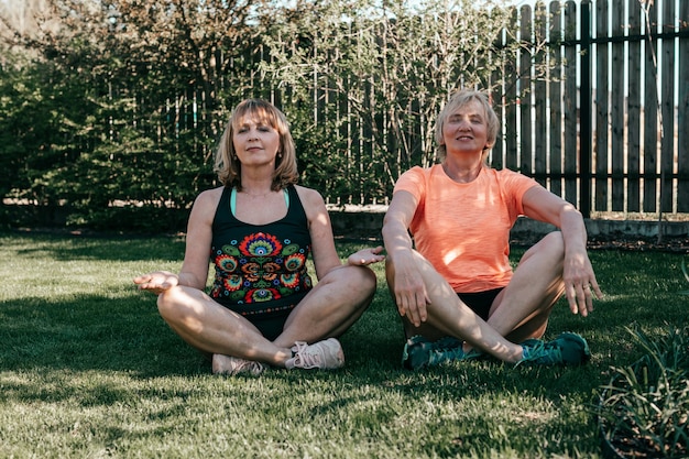 Ritratto di stile di vita delle donne anziane durante lo yoga in natura. Meditazione di due donne nella posizione del loto all'aperto
