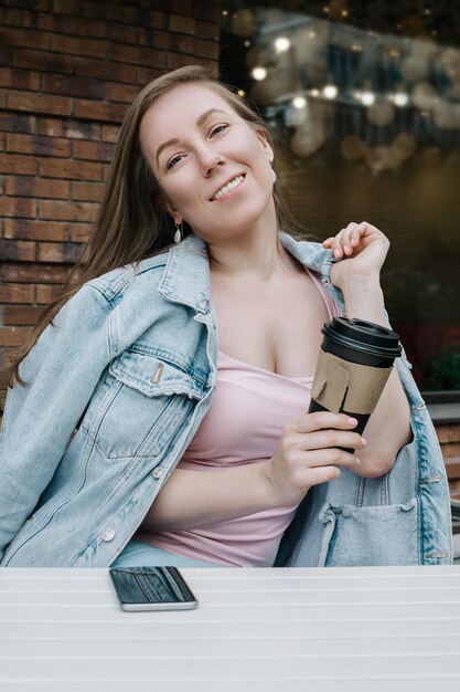 Ritratto di stile di vita di giovane donna bianca adulta che tiene la tazza di caffè da portar via all'aperto, fuoco selettivo