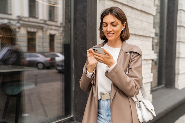 Ritratto di stile di vita di strada di elegante donna bruna di affari europei in cappotto di pelle in posa all'aperto