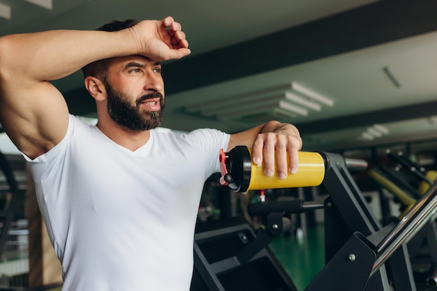 Ritratto di stile di vita di un bell'uomo muscoloso in piedi con lo shaker dopo l'allenamento nella palestra sportiva