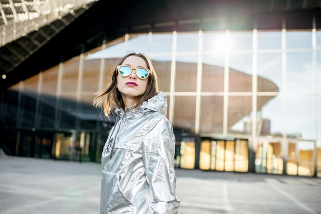 Ritratto di stile di vita di una donna elegante in giacca d'argento che cammina all'aperto sullo sfondo architettonico moderno