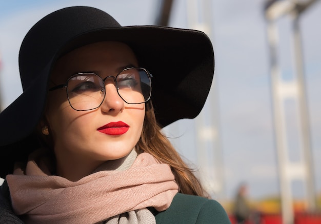 Ritratto di stile di vita di una giovane modella fantastica in posa sul ponte. Donna che indossa cappello, sciarpa e occhiali alla moda