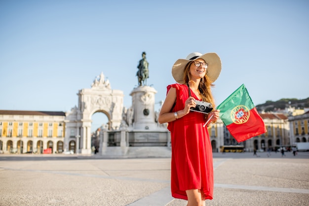 Ritratto di stile di vita di una giovane turista con bandiera portoghese in piedi sulla piazza principale durante la luce del mattino nella città di Lisbona, Portogallo