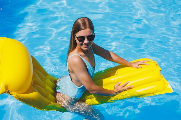 Ritratto di stile di vita estivo di bella donna con occhiali da sole che galleggia su un materasso gonfiabile nella piscina all'aperto Vacanze estive su un'isola tropicale