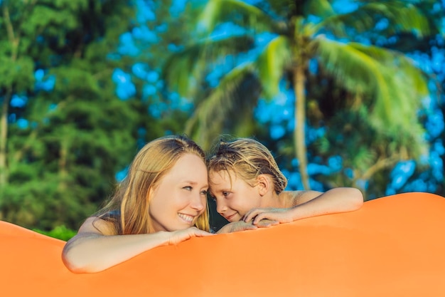 Ritratto di stile di vita estivo di madre e figlio seduti sul divano gonfiabile arancione sulla spiaggia dell'isola tropicale Rilassarsi e godersi la vita sul letto ad aria