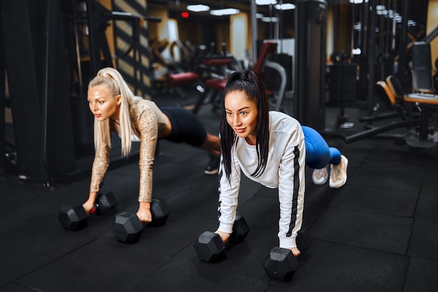 Ritratto di stile di vita sano di due giovani ragazze atletiche che fanno plancia in palestra