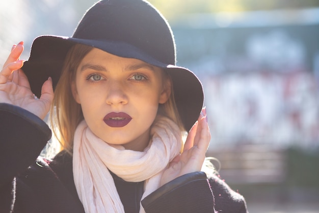 Ritratto di strada di donna bionda affascinante in cappello in posa con riflessi dorati del sole. Spazio per il testo