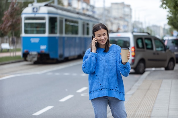 Ritratto di strada di una giovane donna che parla al telefono in città vicino alla carreggiata.