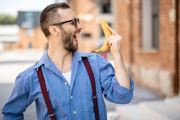 Ritratto di strano uomo d'affari alla moda con banana all'aperto