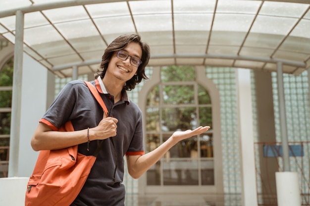 Ritratto di studente felice e sorridente che mostra lo spazio della copia nel cortile anteriore del campus