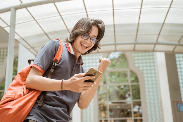 Ritratto di studente molto felice e sorridente che guarda cellulare sul cortile del campus