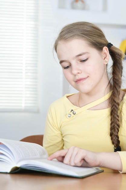 Ritratto di studentessa carina seduta a tavola e leggere