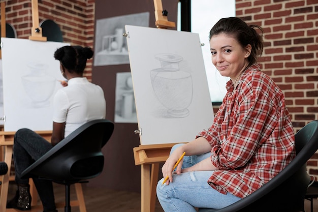 Ritratto di studentessa che lavora al capolavoro dell'illustrazione che disegna il modello del vaso su tela di pittura che lavora alla tecnica grafica usando gli strumenti di disegno nello studio di creatività. Concetto di classe d'arte