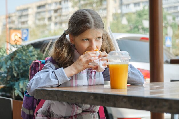 Ritratto di studentessa con zaino, mangiare hamburger con succo d'arancia