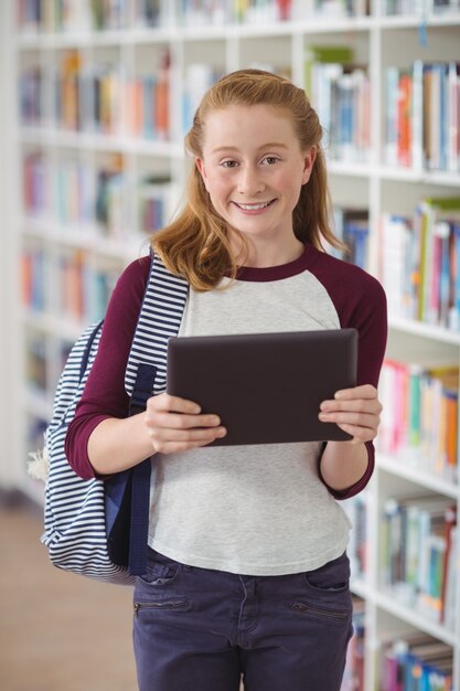 Ritratto di studentessa felice che tiene compressa digitale in libreria