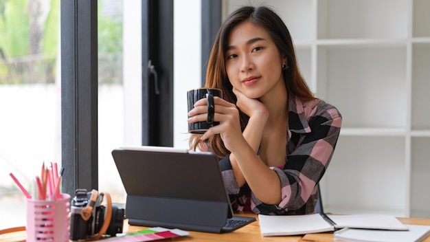 Ritratto di studentessa sorridendo alla telecamera mentre si beve pausa caffè mentre si fa assegnazione in soggiorno