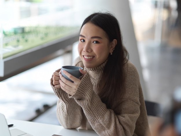 Ritratto di studentessa tenendo la tazza di caffè mentre si è rilassati seduti nella caffetteria