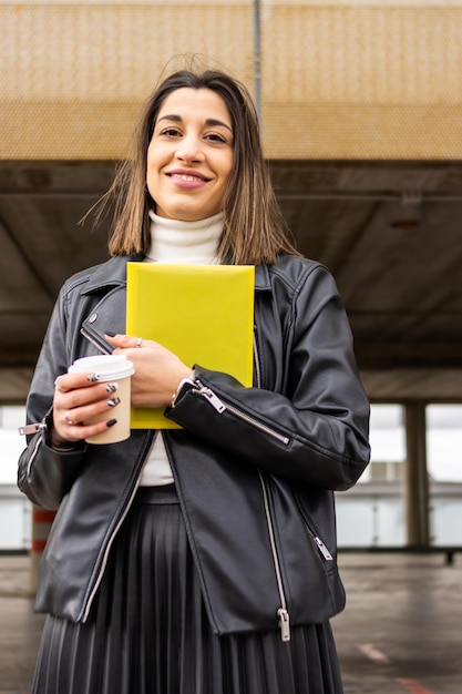 Ritratto di studentessa universitaria sorridente con caffè e documenti all'aperto