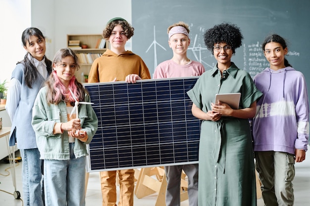 Ritratto di studenti che sorridono alla macchina fotografica mentre imparano il lavoro del pannello solare insieme all'insegnante