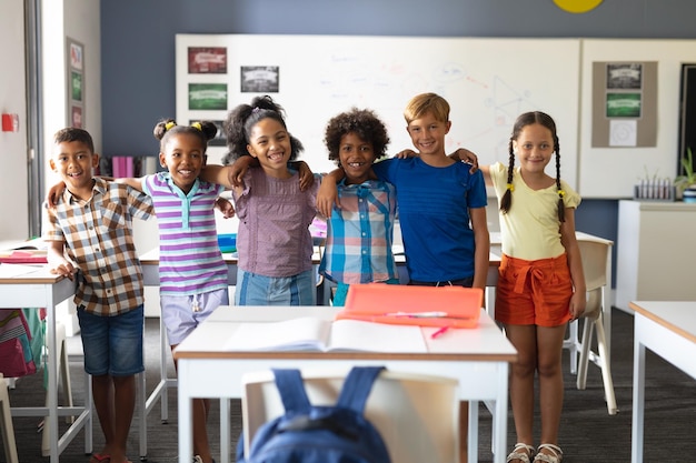 Ritratto di studenti delle scuole elementari multirazziali sorridenti in piedi con le braccia attorno in classe