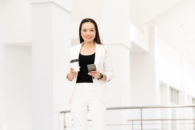 Ritratto di successo Una donna d'affari asiatica di mezza età che tiene in mano uno smartphone e un caffè che sorride alla telecamera