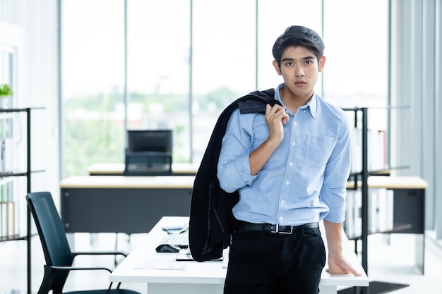 Ritratto di successo vincitore del sentimento bel giovane uomo d'affari asiatico sullo sfondo della stanza dell'ufficio, gli occhi laterali che guardano la telecamera