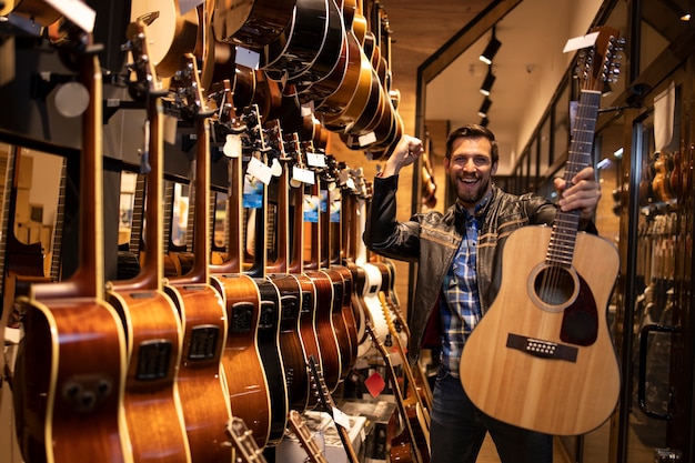 Ritratto di talentuoso musicista caucasico in giacca di pelle che ha appena acquistato una chitarra acustica classica in un negozio di musica.