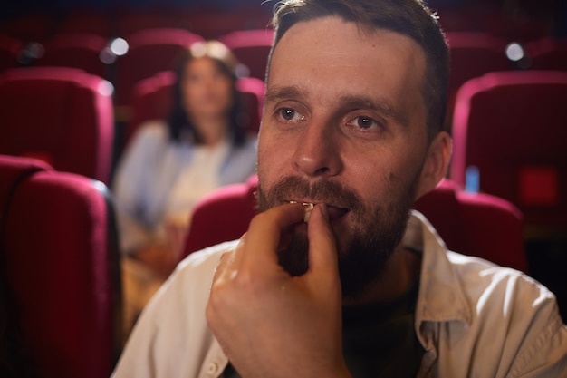 Ritratto di testa e spalle dell'uomo maturo che mangia popcorn nel cinema mentre si gode il film da solo, copia dello spazio