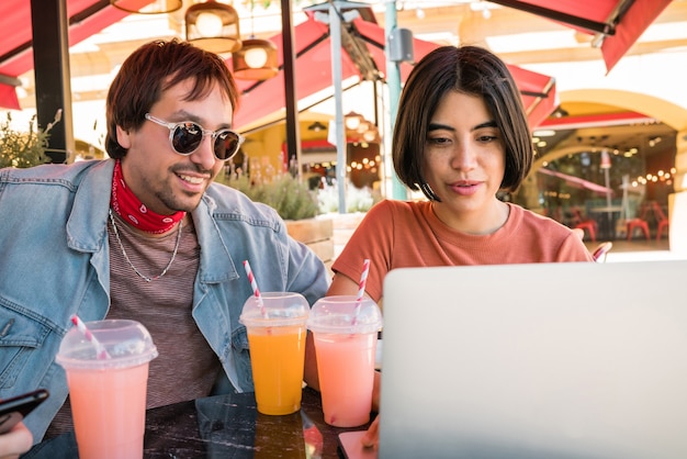 Ritratto di tre giovani amici utilizzando un computer portatile mentre è seduto all'aperto presso la caffetteria. Amicizia e concetto di tecnologia.