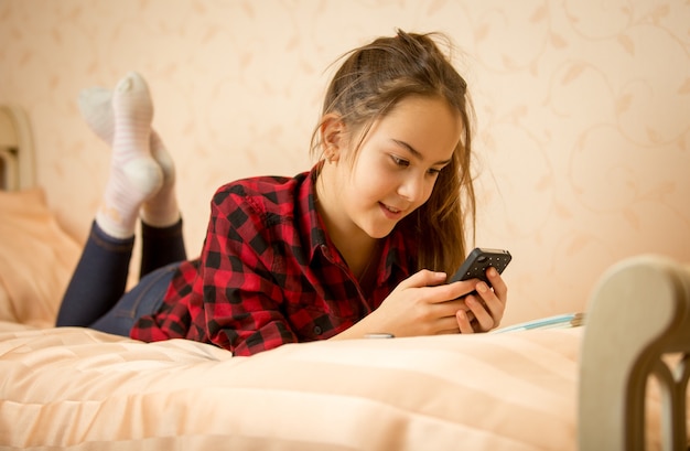 Ritratto di un'adolescente carina sdraiata sul letto e che scrive un messaggio sul telefono